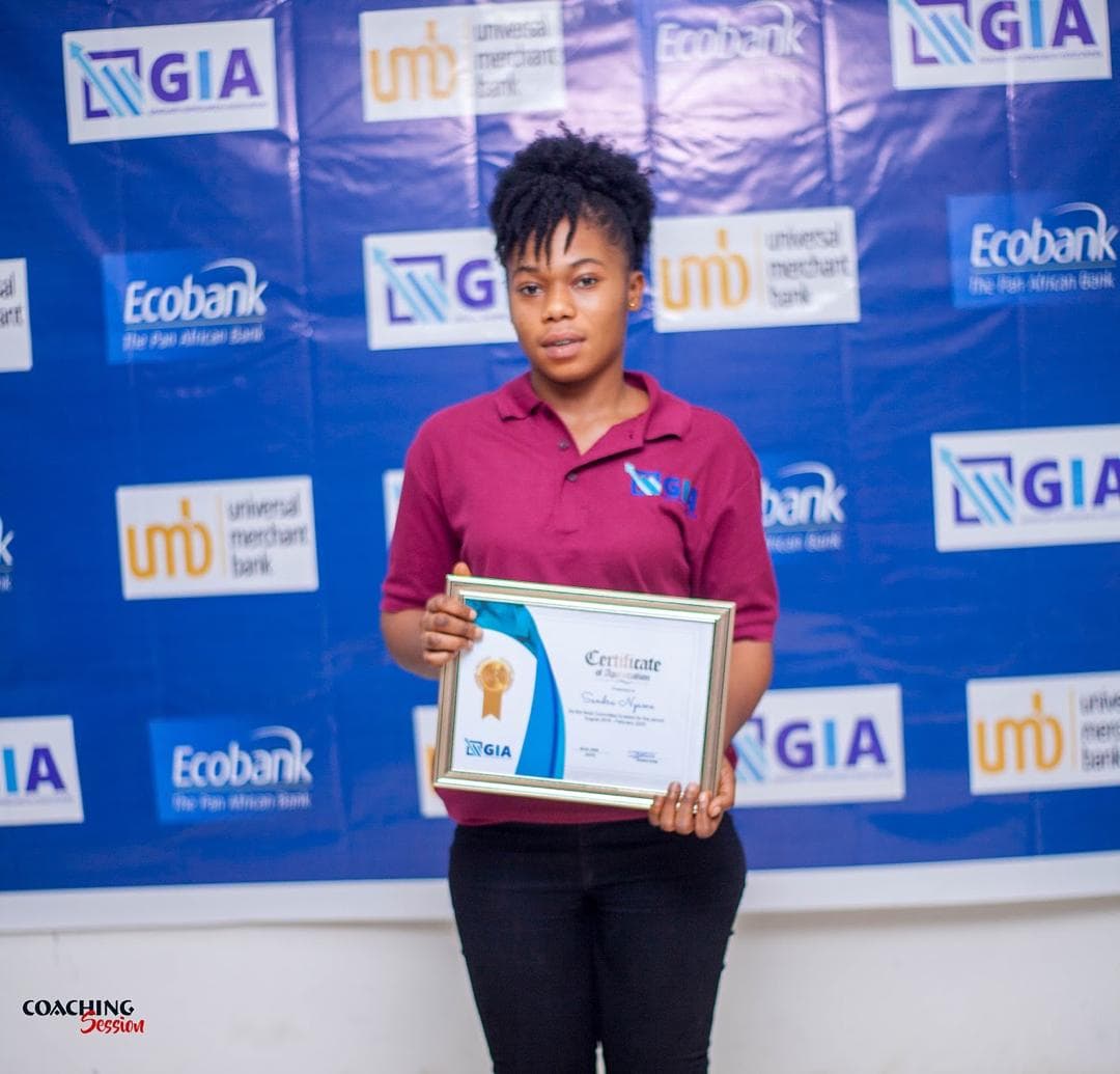 A GIA member holding an award certificate in front of the sponsors' backdrop